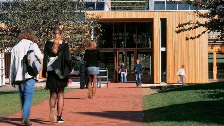Pupils walking towards a timber-clad building on the Bedales School campus